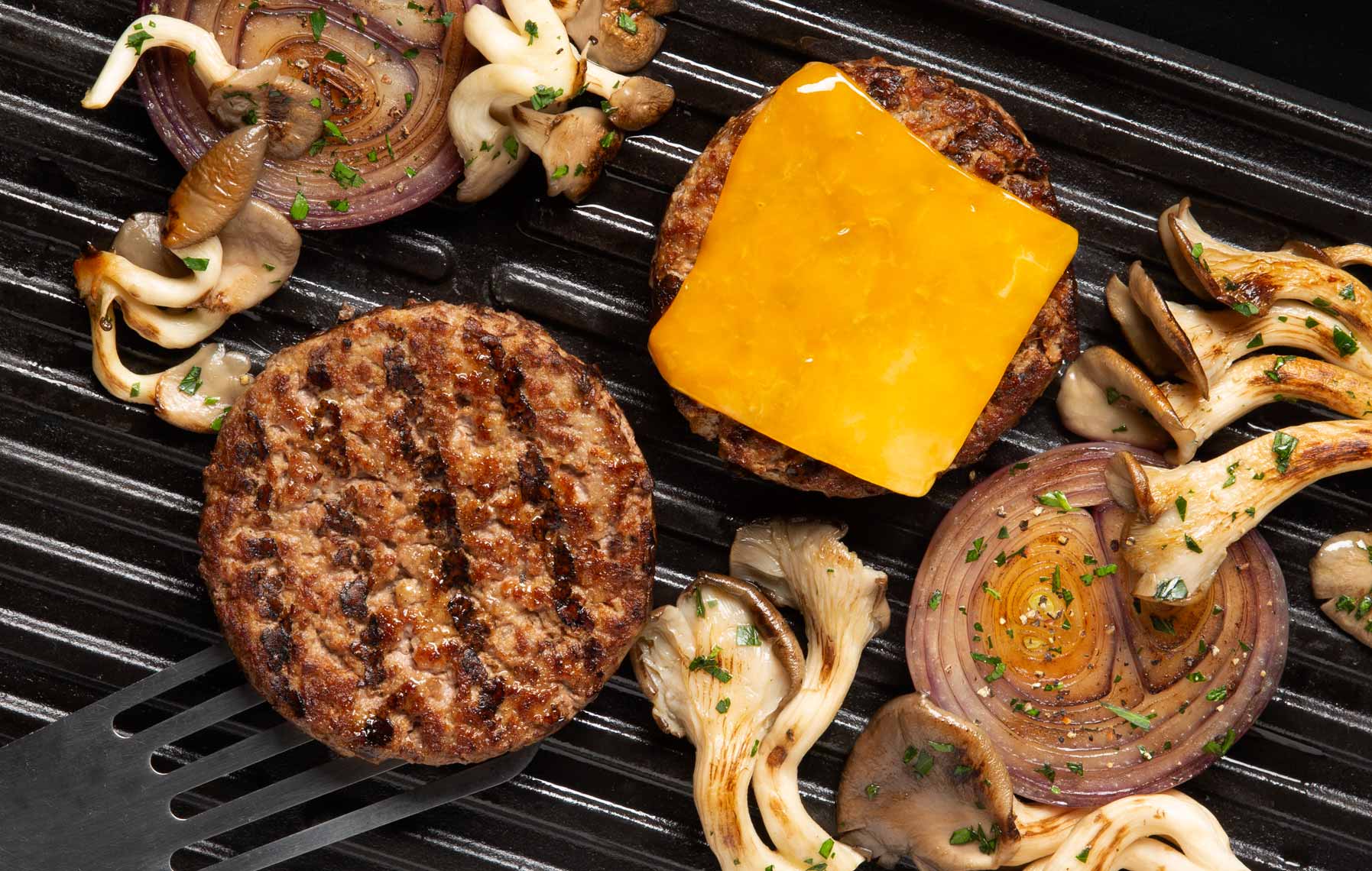 Hamburger patty on grill with cheese and shitake mushrooms